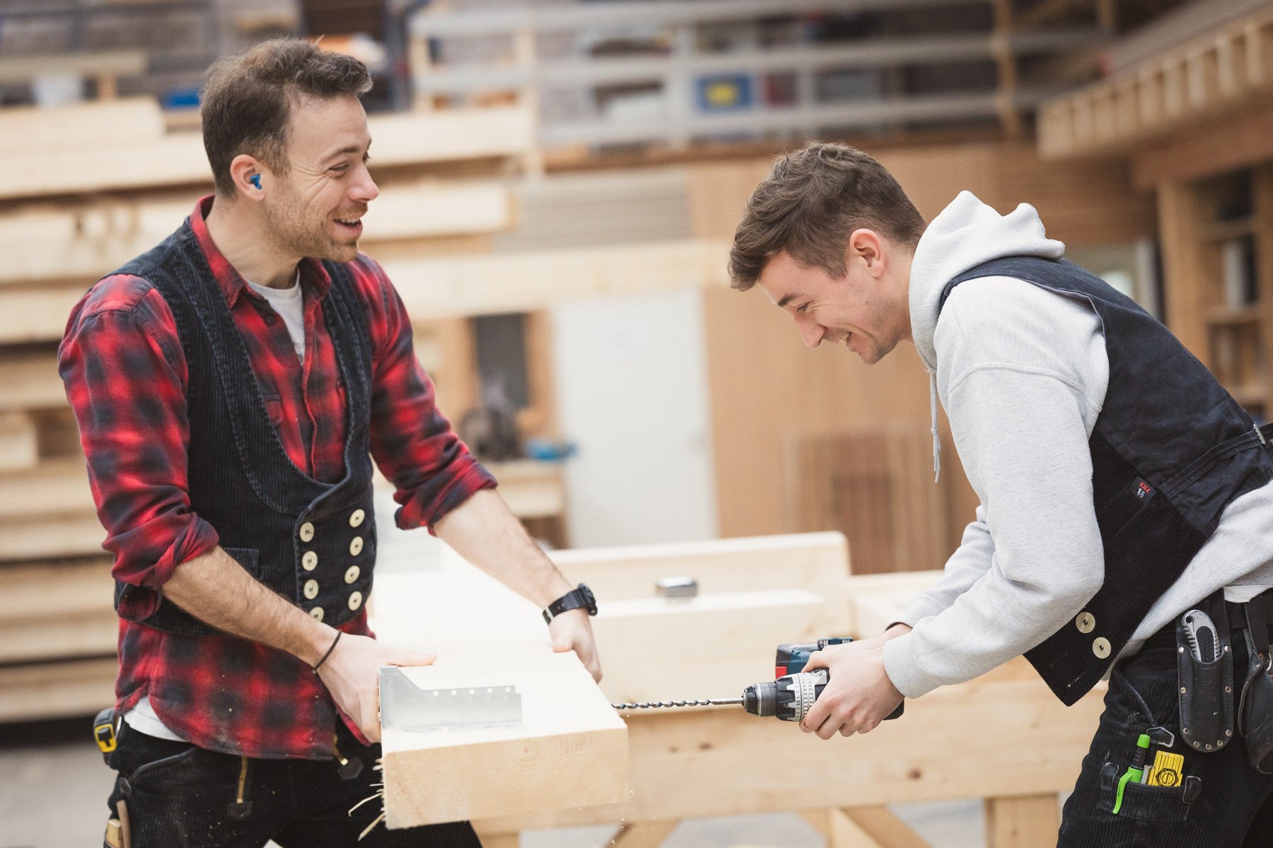 Lukas und Marco lachen bei der gemeinsamen Arbeit an einem Holzbalken
